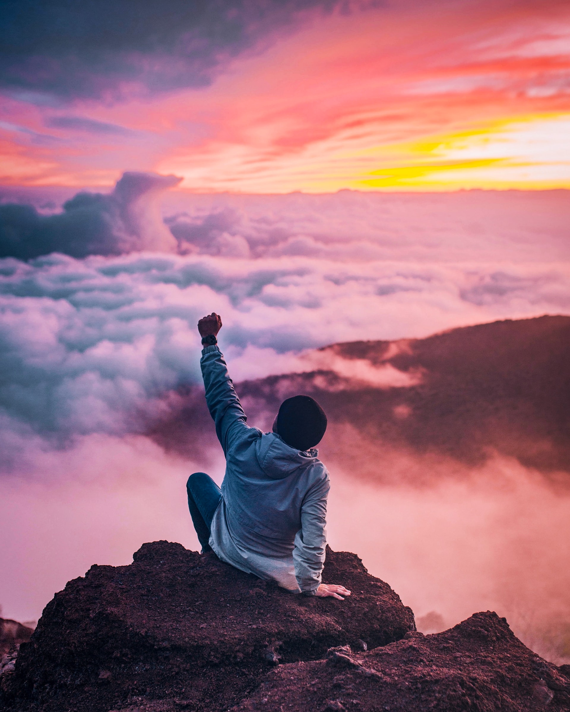 a man sitting on top of a mountaing with his hand raised